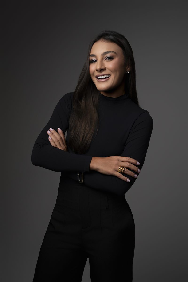 Dra. Ana Carolina de Castro sorrindo, em retrato de estúdio sobre fundo escuro.